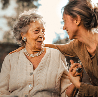 female unpaid family carer supporting elderly mother. Both ladies smiling.